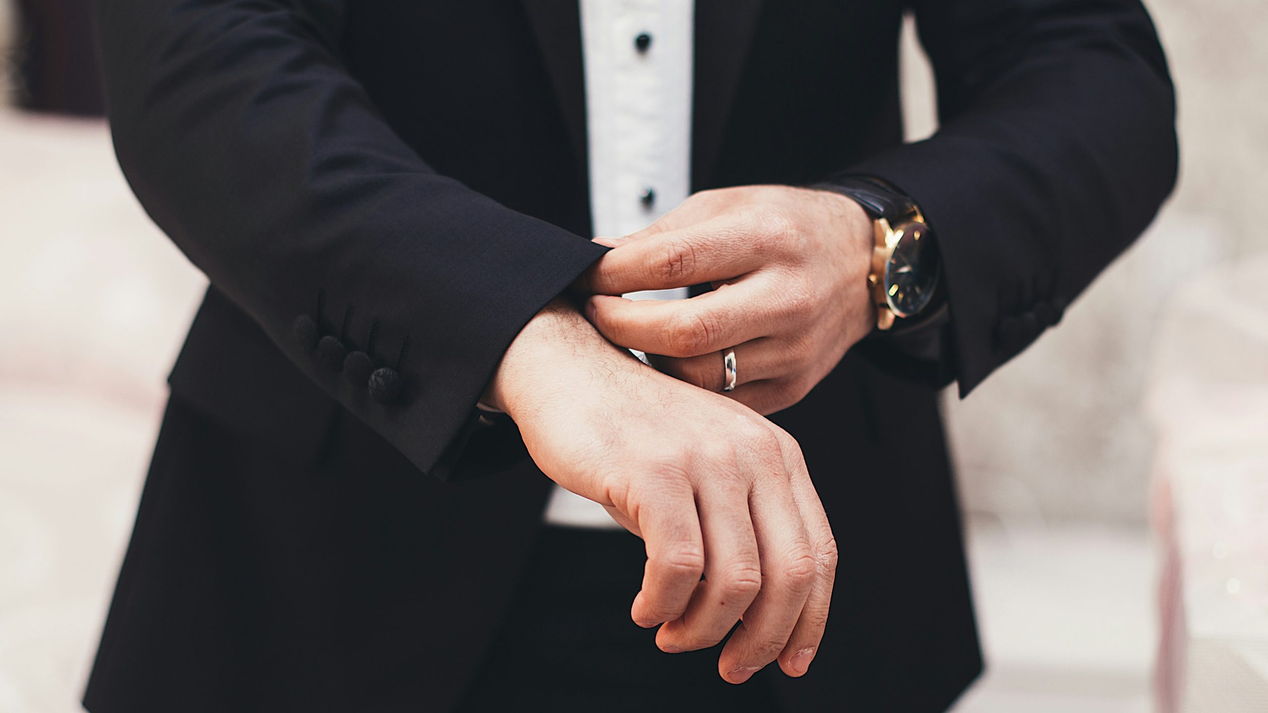 A man testing the fit of his suit jacket after learning how to measure himself. The suit is black, with a white undershirt, and a watch on his wrist.