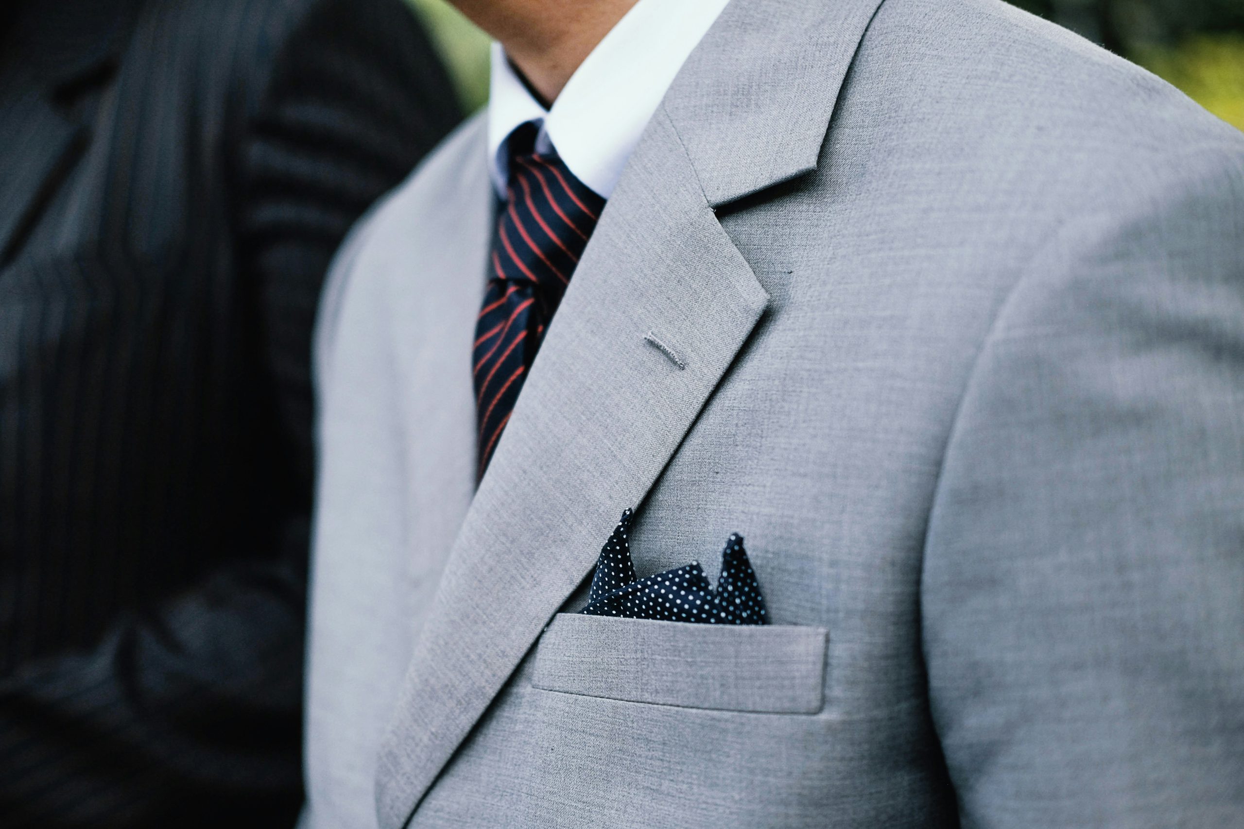 A man wearing a grey linen suit with a tie, button square, and a white shirt.