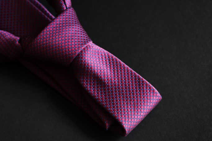 A purple tie with blue crosshatching sits on a black background. The tie is a windsor knot.