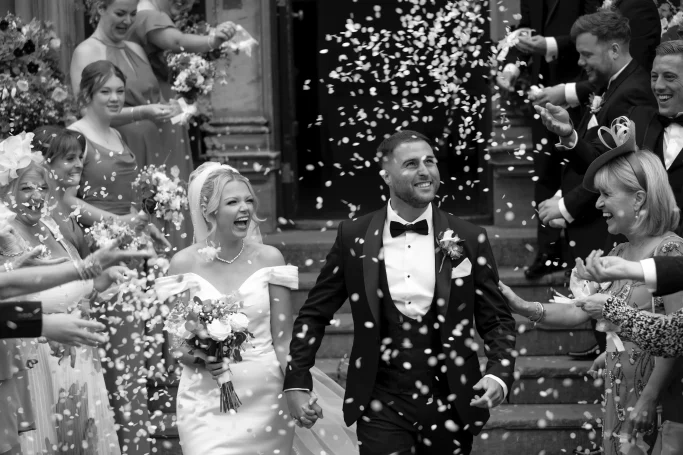 A married couple leaving the church in monochrome, with confetti showering to them.